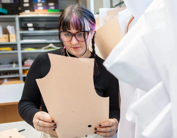 A fashion student examining a paper pattern for garment design in a sewing studio. A fashion student examining a paper pattern for garment design in a sewing studio.